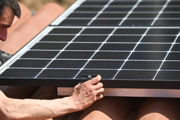 Bina işçisi çatıda tornavidayla alternatif enerji fotovoltaik güneş panellerini tamir ediyor.