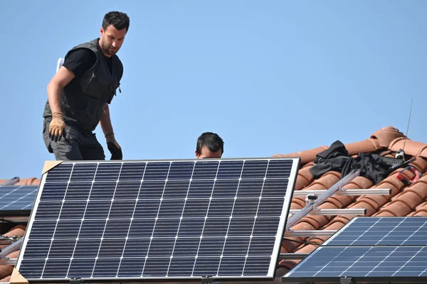 building worker installing solar panels on roof of individual house
