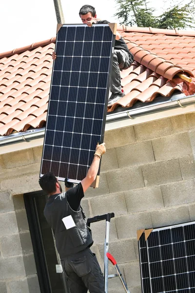 Workers installing solar panels on residential house roof with red tiles