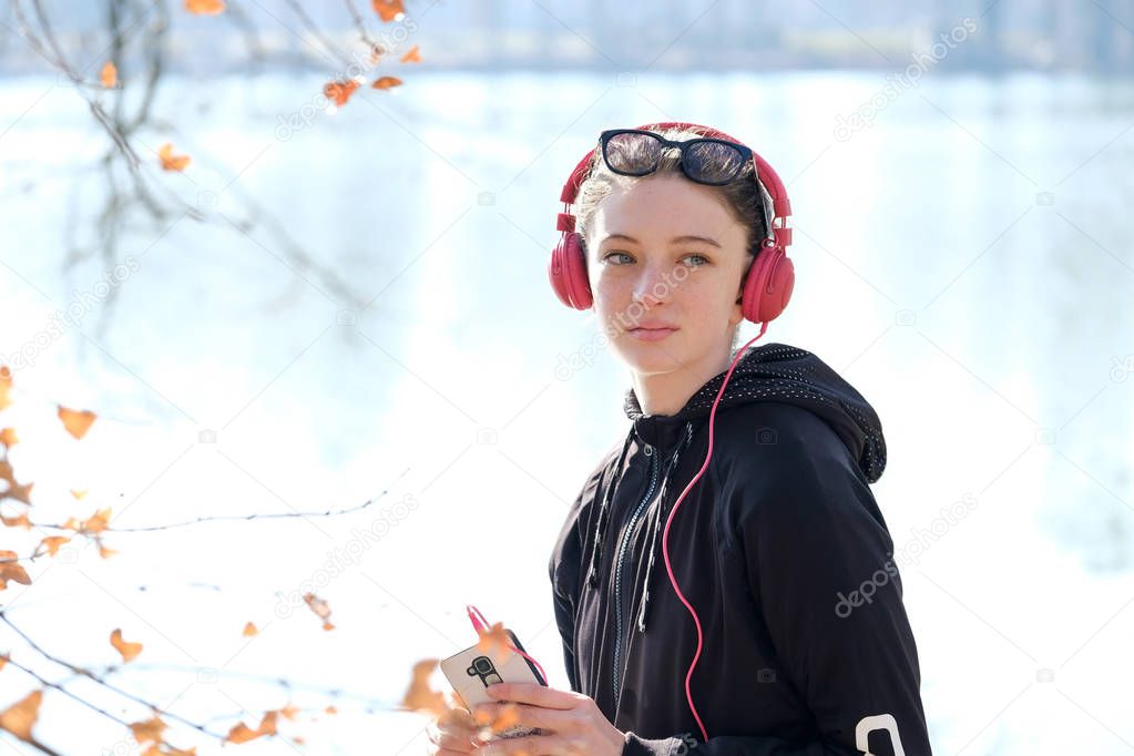  smiling teenager girl with pink headset and solar sunglasses listen to music on a mobile