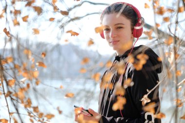  Pembe kulaklıklı gülümseyen genç kız cep telefonundan müzik dinliyor.