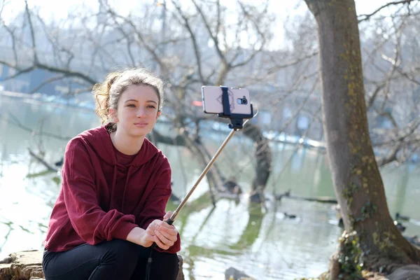 Nastolatek dziewczyna co zdjęcia z selfie kij na zewnątrz w pobliżu jeziora — Zdjęcie stockowe
