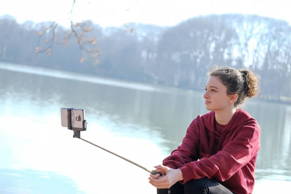Nastolatek dziewczyna co zdjęcia z selfie kij na zewnątrz w pobliżu jeziora — Zdjęcie stockowe