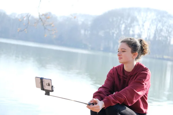 Nastolatek dziewczyna co zdjęcia z selfie kij na zewnątrz w pobliżu jeziora — Zdjęcie stockowe