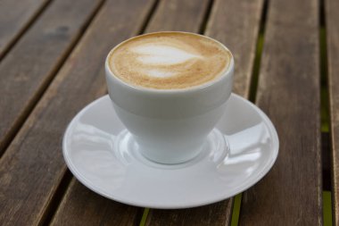 Ahşap bir masada bir kupa lezzetli kapuçino..