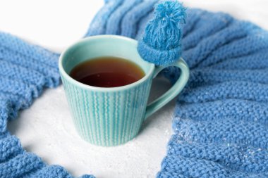 Kış konsepti. Mavi beyaz renk . Bir fincan sıcak çay, örgü bir atkı ve beyaz backgroung üzerinde küçük bir şapka ile tatlandırılmış. Soğuk renk.