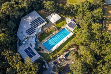 Sydney, Avustralya: 26 Haziran 2020: Açık havada olimpiyat büyüklüğünde, altı şeritli, ağaçlarla çevrili bir spor salonunda yüzme havuzu ve insanların yüzme turları attığı öğleden sonra güneşli bir parkta yüzme sahnesi