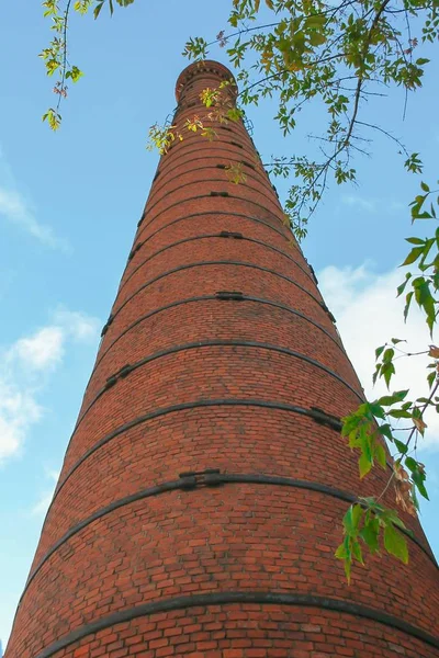 Old brick pipe factory against a blue sky and green leaves.