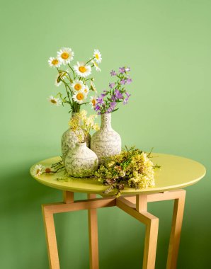 Masasında kır çiçekleri olan üç seramik vazo.