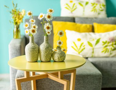 Kanepenin önündeki masanın üzerinde papatya olan seramik vazolar..