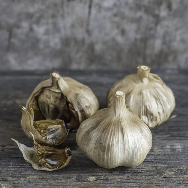 black garlic bulbs and cloves on a rustic wooden table with textured background, moody product photo, food image with negative space for title