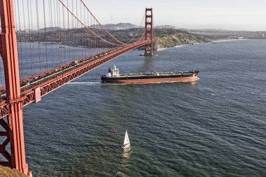 Gün batımında hızlı hareket eden kargo konteyner gemisi, San Francisco Körfezi'nden ayrılarak Golden Gate Köprüsü'nün altından geçerek, Marin County'deki Horseshoe körfezinden fotoğraflandı, Fort Baker yakınlarında.