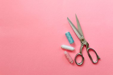 Mavi ve pembe arka plan üzerine dikiş iplikleri ve makaslar.