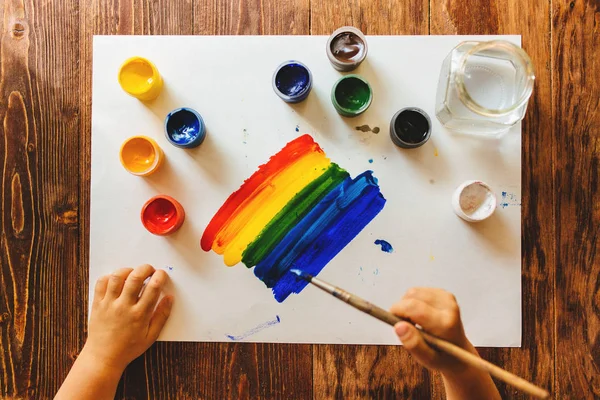 Niño dibuja pintura gouache en una hoja de papel arco iris . — Foto de Stock