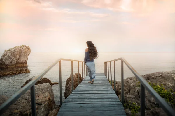 Mulher caminha na ponte contra o fundo do pôr do sol mar . — Fotografia de Stock