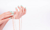 Ruce mladé dívky, manikúra na módním pozadí, zelený lak, perlové korálky