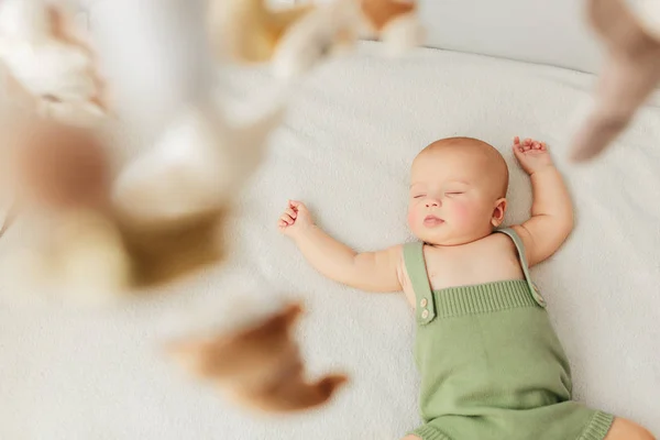 Pequena menina dorme em uma cama em um terno verde playmobile gira sobre ela . — Fotografia de Stock