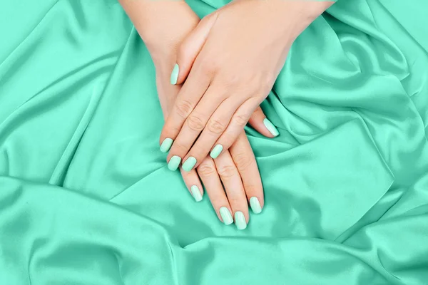 Hands of a young girl on a mint silk cloth, manicure on a trendy background , green polish. — Stock Photo, Image