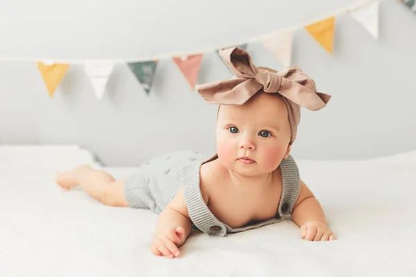 Belo bebê jaz na cama sorrindo arco em sua cabeça . — Fotografia de Stock