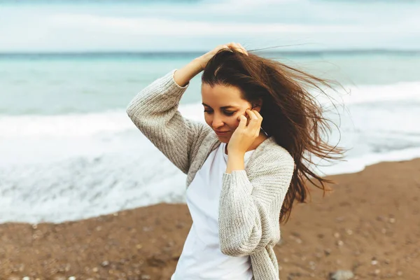 Una hermosa joven camina a lo largo de la orilla del mar, una tormenta, el pelo vuela aparte, un cárdigan gris, una figura deportiva en zapatillas de deporte disfruta, otoño o invierno — Foto de Stock