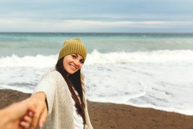 Güzel bir genç kız deniz kıyısı boyunca yürür, bir fırtına, saç ayrı sinek, gri bir hırka, spor figürü spor figürü sahiptir, sonbahar veya kış