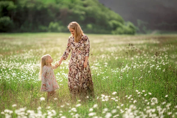 Hermosa madre joven con su hija en un campo con margaritas sol puesta del sol, estilo de vida, concepto de maternidad, caminar en el parque o en la naturaleza —  Fotos de Stock