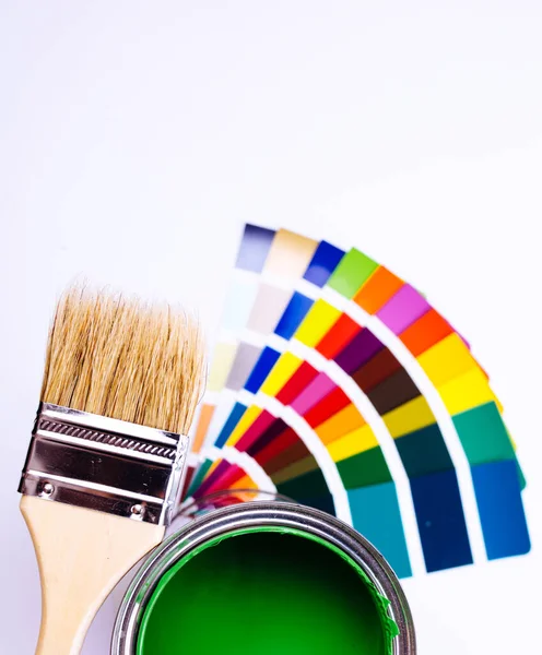 페인트 솔을 여러 가지 색깔 표본 위에 놓으라. 녹색 페인트 캔 이 활짝 열려 있다 — 스톡 사진