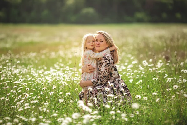 Schöne junge Mutter mit ihrer Tochter auf einem Feld mit Gänseblümchen Sonnenuntergang Sonne, Lebensstil, Konzept der Mutterschaft, Spaziergang im Park oder in der Natur — Stockfoto