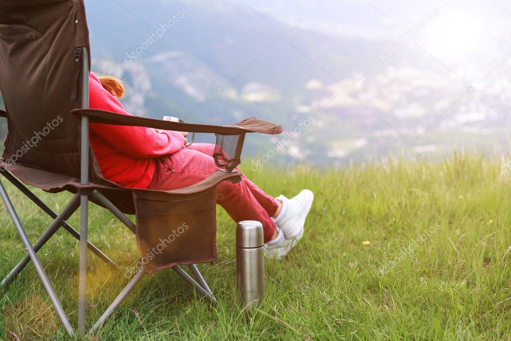 Closeup photo of cup with tea in travelers hand over out of focus mountains view. A young tourist woman drinks a hot drink from a cup and enjoys the scenery in the mountains. Trekking concept.