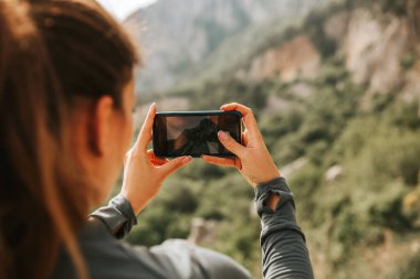 Gezgin kadın dağın yakınında oturuyor ve uzaklara bakıyor, fotoğraf çekiyor bahar havası, sakin manzara. Açık havada yürüyüş, güneş ışığında manzara manzarası. Gezgin şehvetinin bir dizi fotoğrafı..