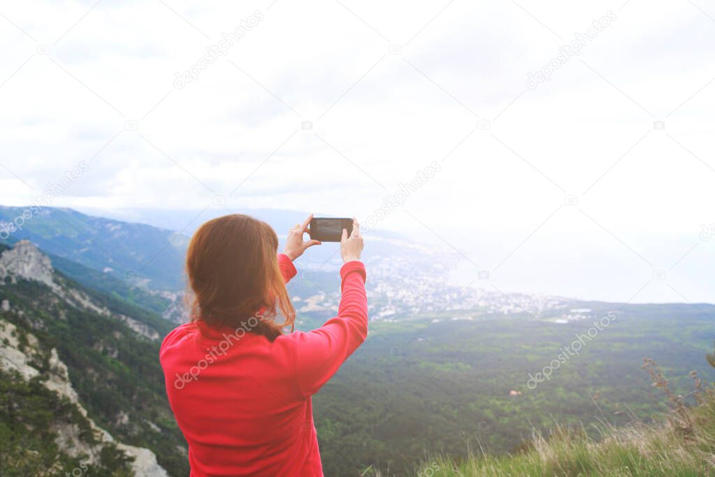 Closeup photo of cup with tea in travelers hand over out of focus mountains view. A young tourist woman drinks a hot drink from a cup and enjoys the scenery in the mountains. Trekking concept.