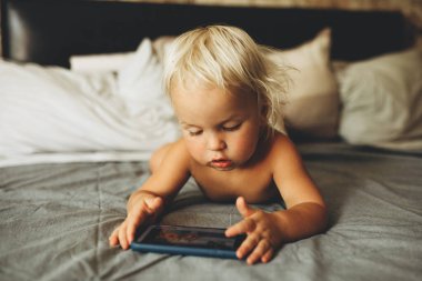 Yatakta uzanmış akıllı telefonu kontrol eden şirin bir bebeğin portresi..