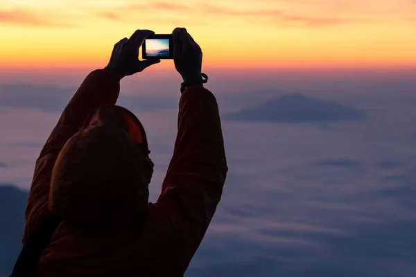 silhouette of person in orange jacket take a photo of sunrise and fog