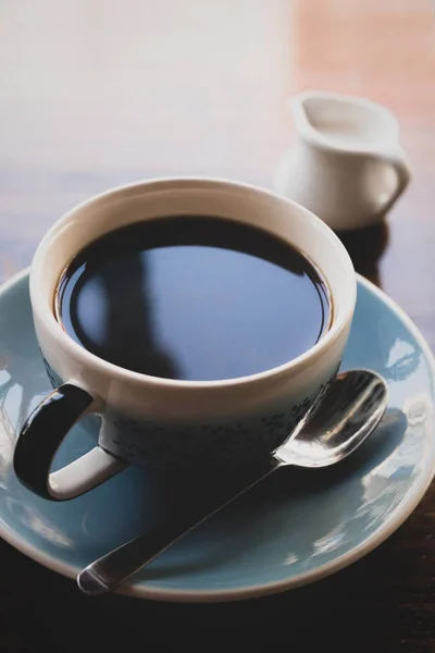 cup of black coffee on table with jug of milk