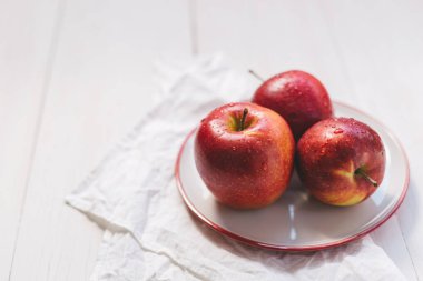 Beyaz bir tabakta üç olgun kırmızı elma.