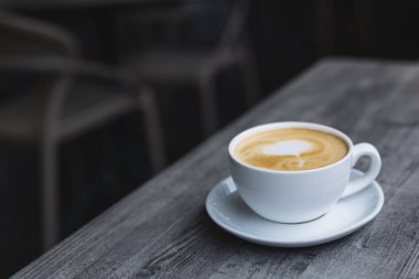 Bir fincan kahve ve ahşap masa üzerinde latte sanatı.