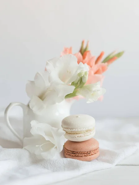 Deux macarons français pastel et des fleurs dans un bocal sur fond blanc . — Photo