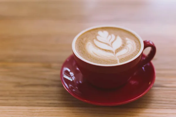Šálek cappuccina s Latte art na dřevěném podkladu. Červený keramický pohár. — Stock fotografie