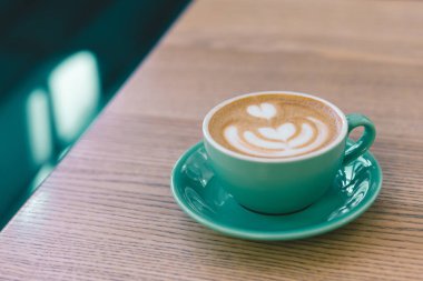 Ahşap arka planda latte sanatıyla kapuçino. Yeşil seramik bardak.