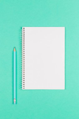 Turkuaz zemin üzerinde boş sayfa ve kalem bulunan defter.