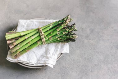 Beyaz peçeteyle servis edilen bir tabak dolusu taze kuşkonmaz. Gri arka plan. Metin için yer.