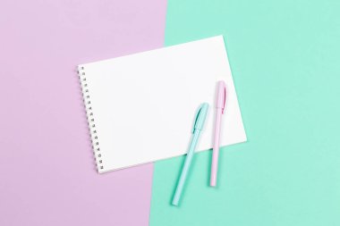 Boş sayfalı bir defter ve menekşe ve turkuaz arka planda iki kalem. Düz yatıyordu. Metin için yer. 