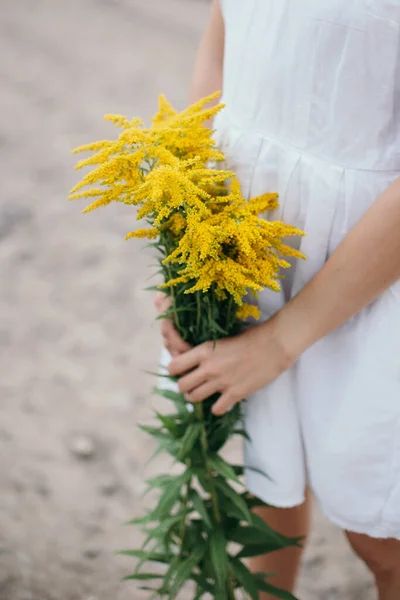 黄色の野花の花束と白いリネンのドレスの女の子 夏の背景 選択的焦点 — ストック写真