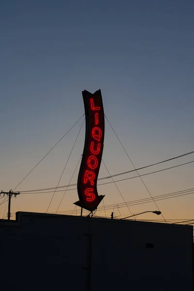 Un letrero rojo de la tienda de licores de neón brillando durante una puesta de sol . — Foto de Stock