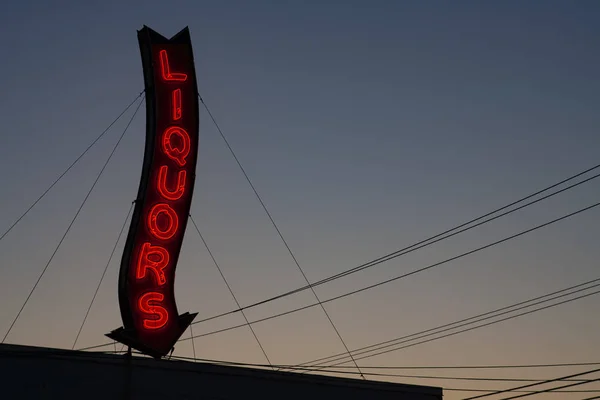 Un letrero rojo de la tienda de licores de neón brillando durante una puesta de sol . — Foto de Stock