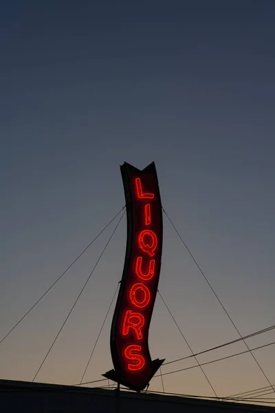 Un letrero rojo de la tienda de licores de neón brillando durante una puesta de sol . — Foto de Stock