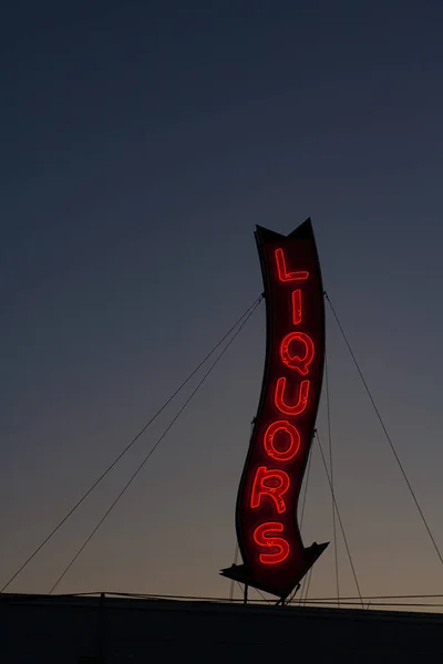 A red neon liquors store sign glowing during a sunset.