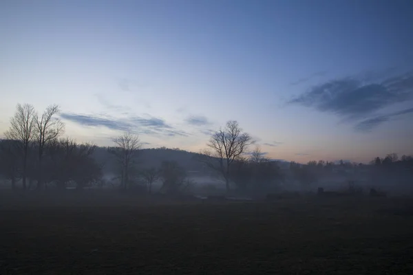 A ghostly fog hovers over farmland along a country road — Stock Photo, Image