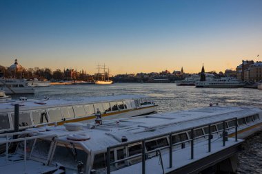 İsveç 'in Stockholm limanındaki bir limana kışın gün batımında yanaşan kar kaplı su taksileri. 