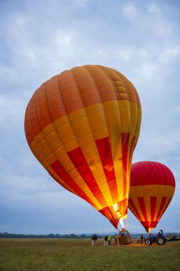 Crews ready hot air balloons before taking to flight during a cloudy morning over the savanna of the Masai Mara National Reserve, Kenya, Africa. Balloons inflating with hot air produced by flames.